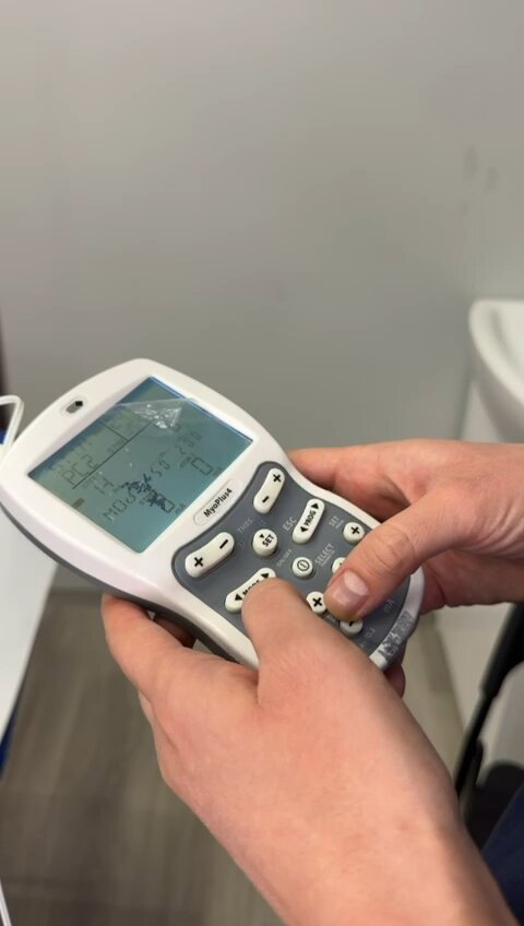 Dłonie fizjoterapeuty ustawiające parametry na aparacie do elektroterapii w gabinecie CRMed
