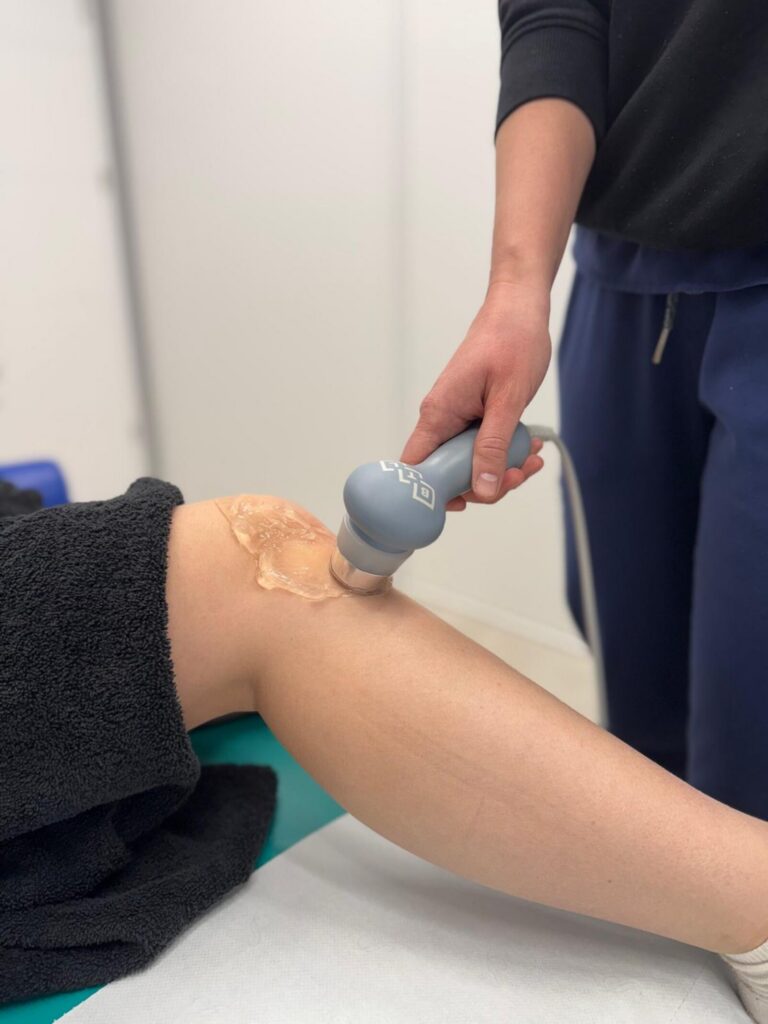 Głowica ultradźwięków z żelem przykładana do kolana pacjenta, dłoń fizjoterapeuty — gabinet CRMed