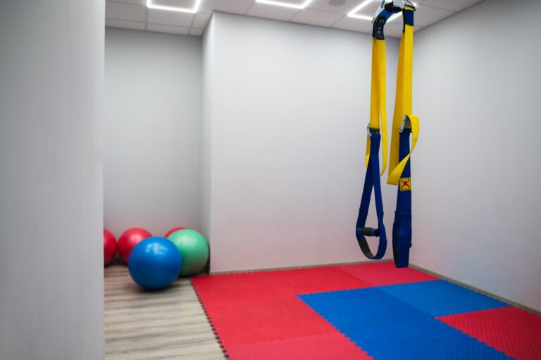 Sala CRMed w Gliwicach: czerwono-niebieskie maty, piłki gimnastyczne w rogu i żółto-niebieskie taśmy TRX